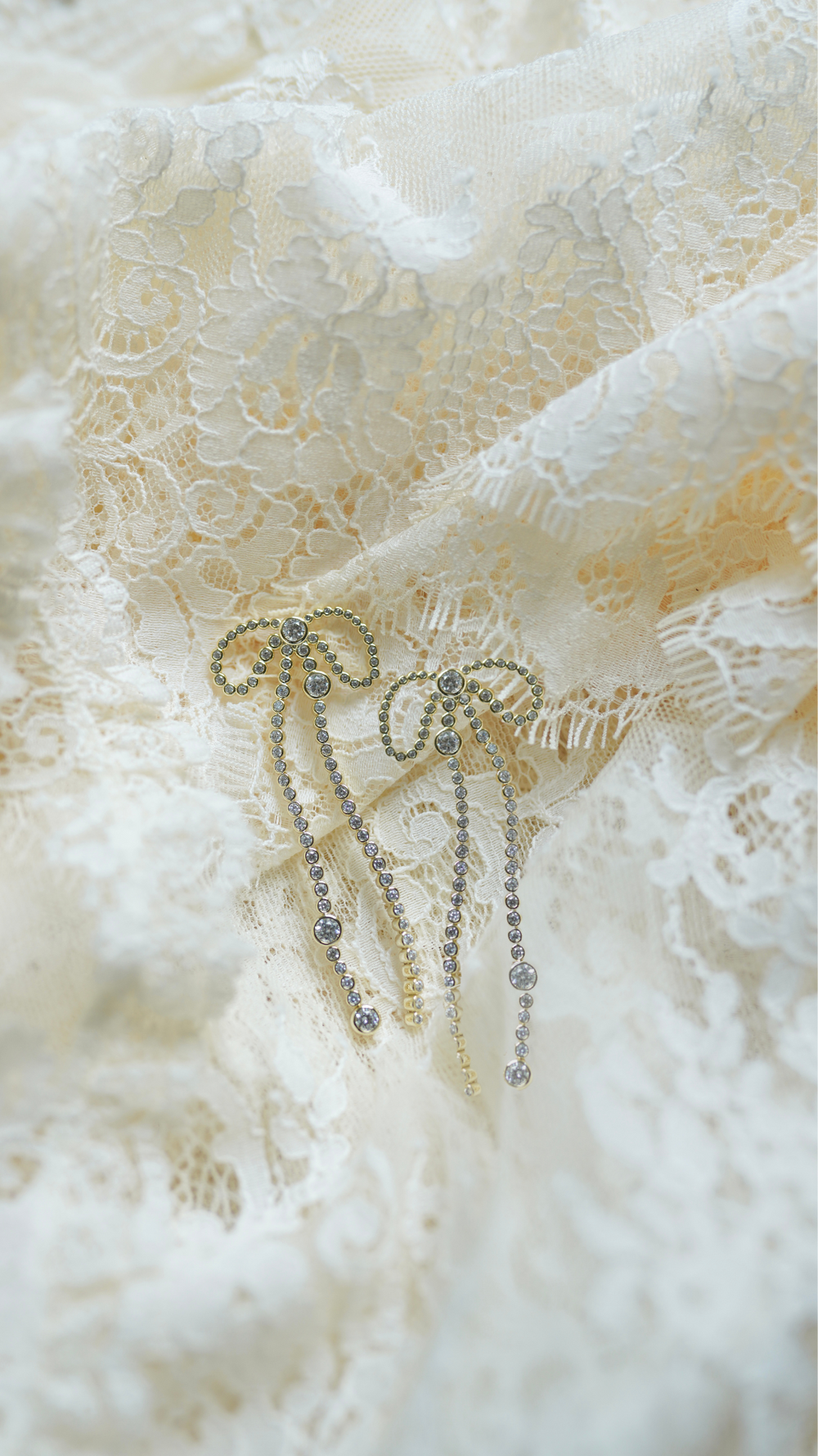 Close up of The Vivienne earrings showing gold plated ribbon bows with cascading crystal strands on ivory lace background