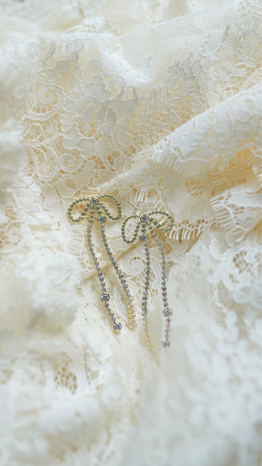 Close up of The Vivienne earrings showing gold plated ribbon bows with cascading crystal strands on ivory lace background