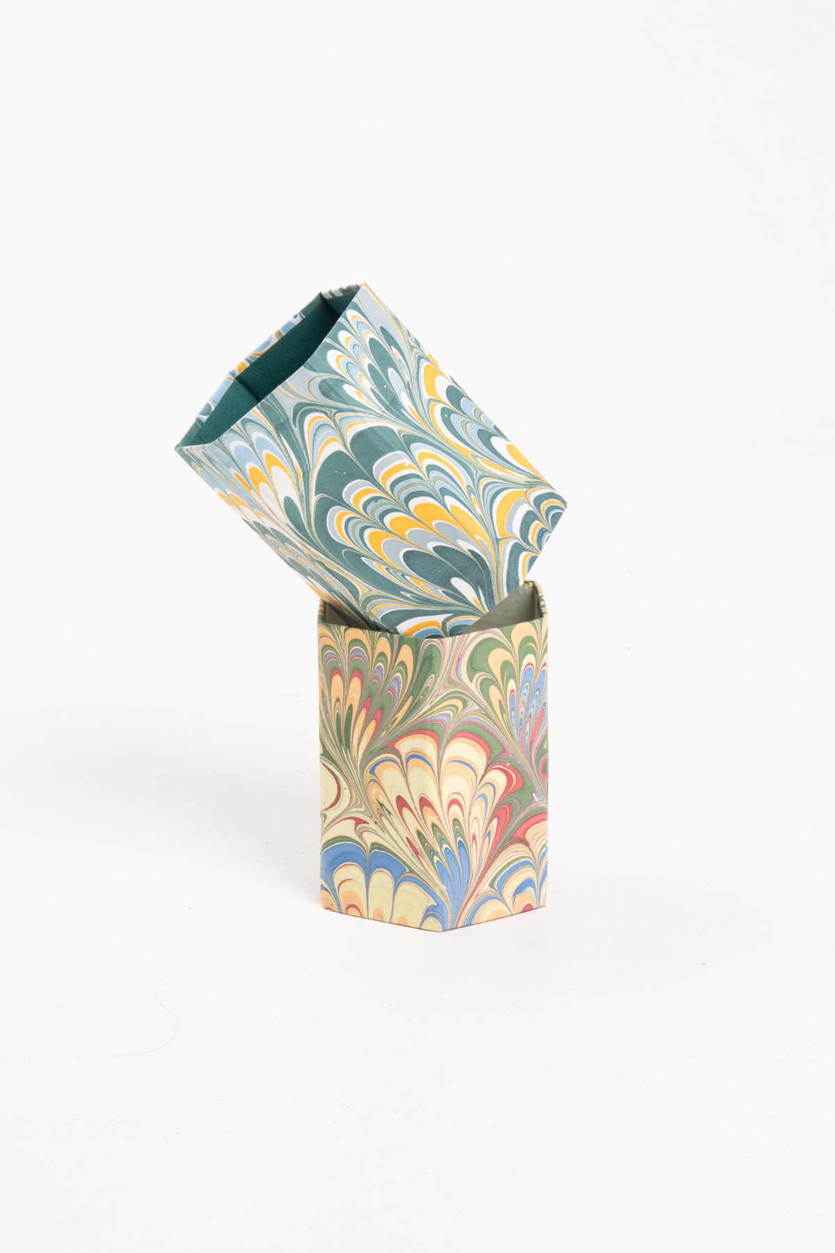 Angled view of two hand-marbled multicolor pencil holders, one tilted inside the other, on white background