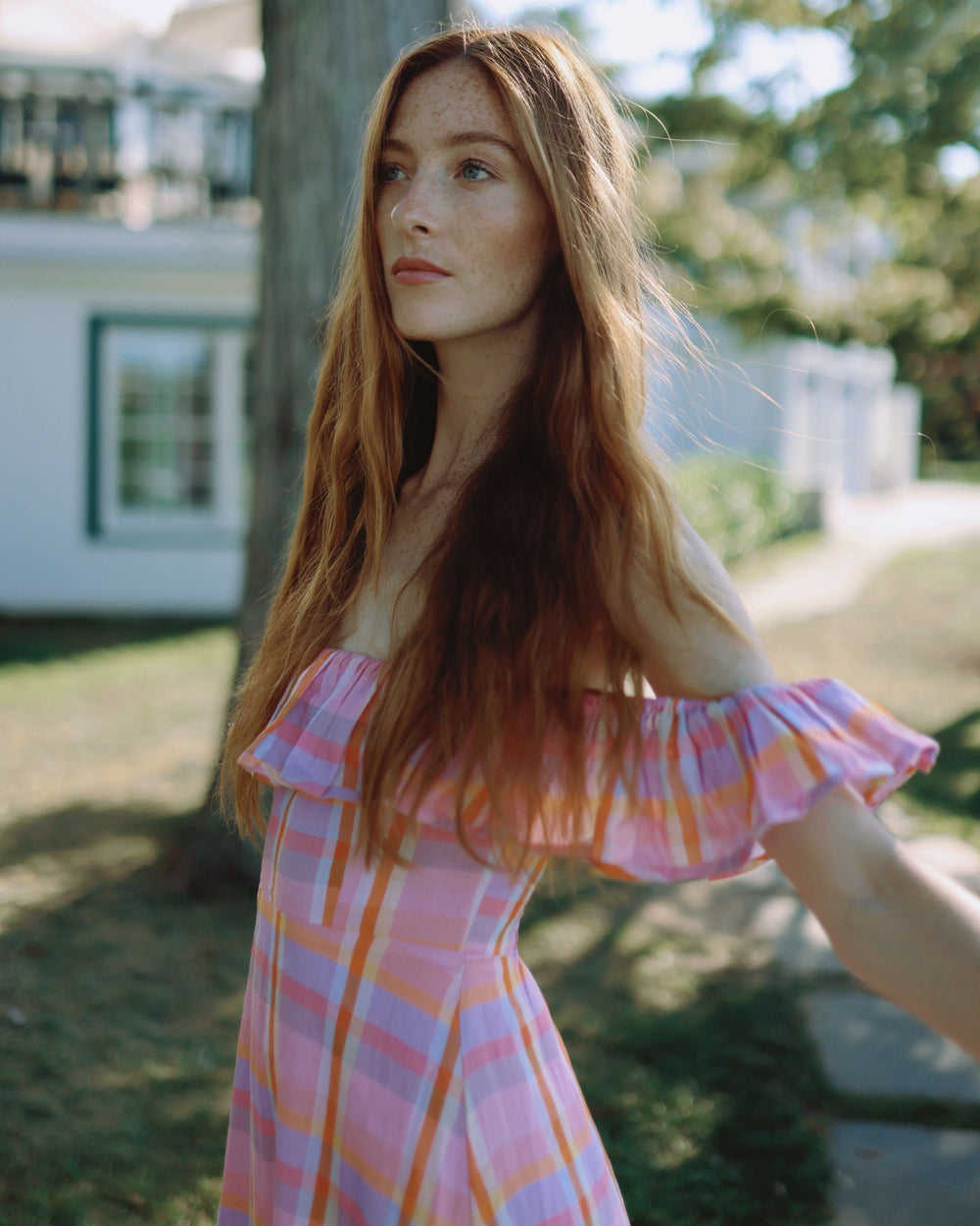 Three-quarter view of Parker Dress in Sherbet Plaid showing off-the-shoulder ruffle and fitted bodice against sunlit yard