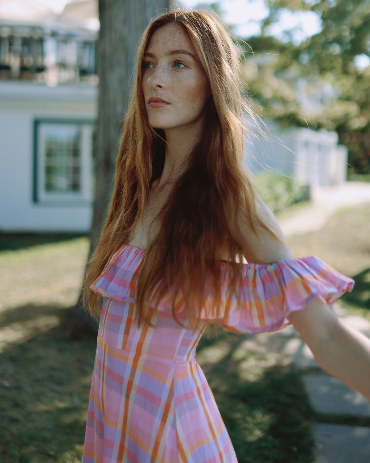 Three-quarter view of Parker Dress in Sherbet Plaid showing off-the-shoulder ruffle and fitted bodice against sunlit yard
