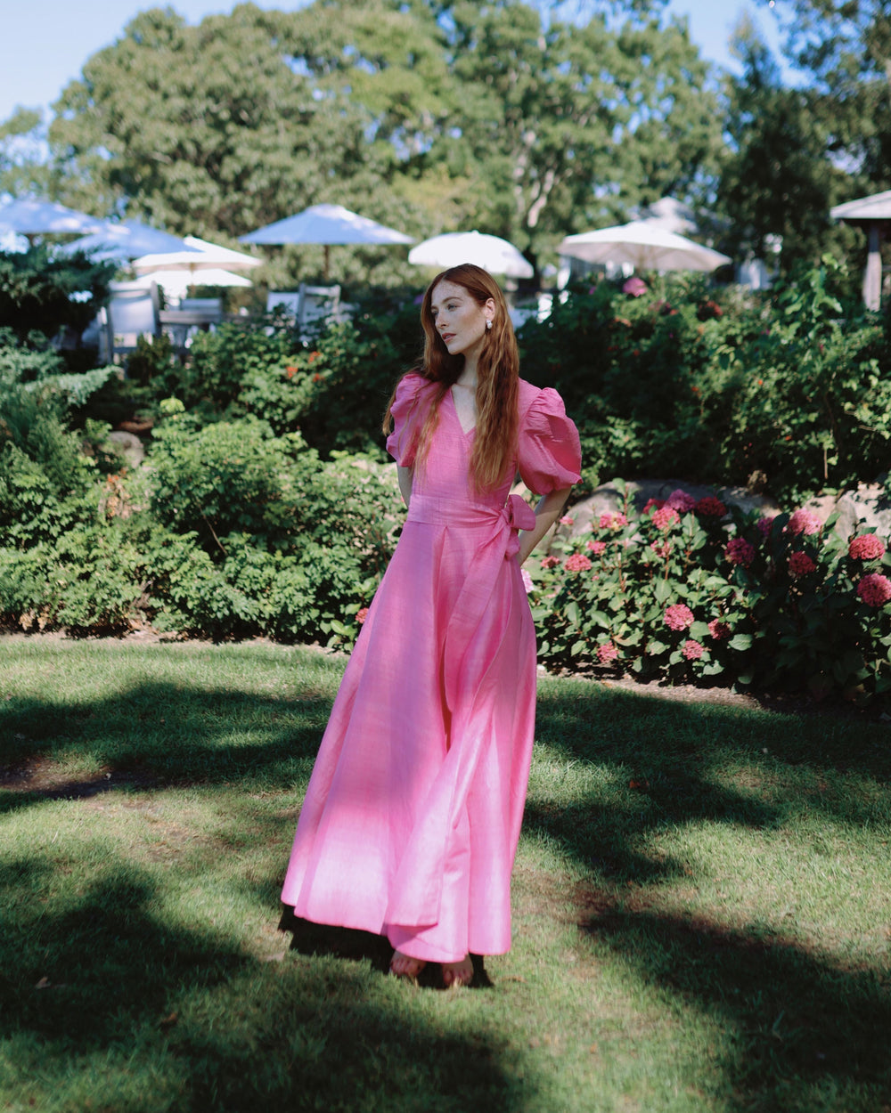 Three quarter view of Kate Maxi Dress in bougainvillea on model showing wrap waist, puff sleeves, and flowing skirt in garden