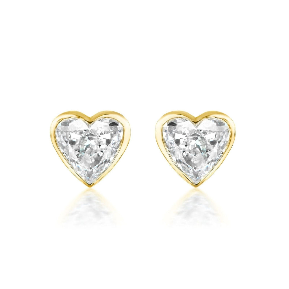 The Bezel Set Diamond Heart Studs showcase G color diamonds in a heart shape, set in 18k gold and displayed on a white background.