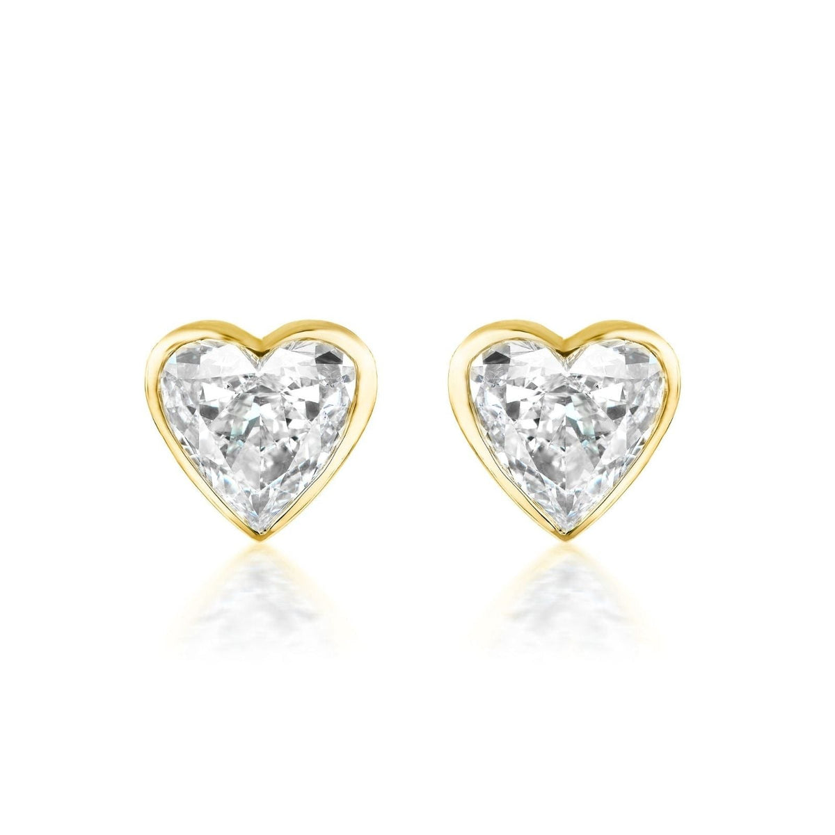 The Bezel Set Diamond Heart Studs showcase G color diamonds in a heart shape, set in 18k gold and displayed on a white background.