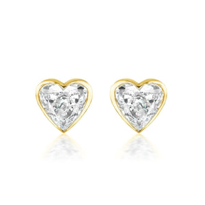 The Bezel Set Diamond Heart Studs showcase G color diamonds in a heart shape, set in 18k gold and displayed on a white background.