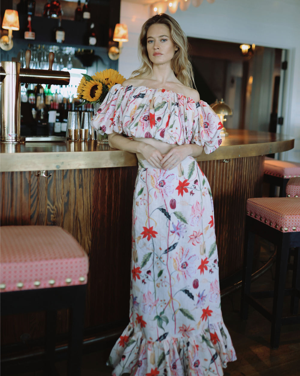Front view of Camilla Set in Wild Jardin showcasing off-the-shoulder puff-sleeve crop top and ruffle-hem maxi skirt at a bar