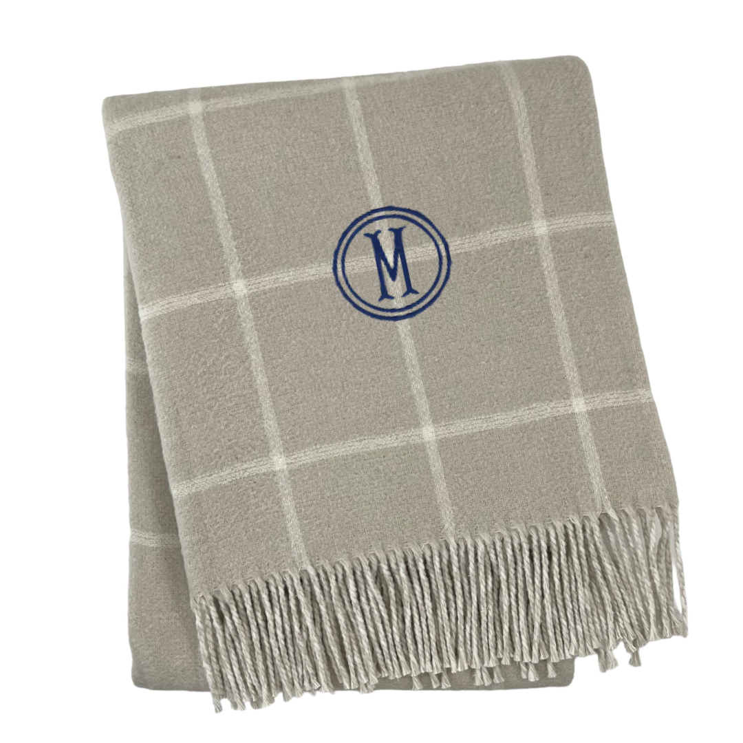 Front view of Windowpane Throw with light gray windowpane pattern, fringed edge, and blue embroidered M on white background