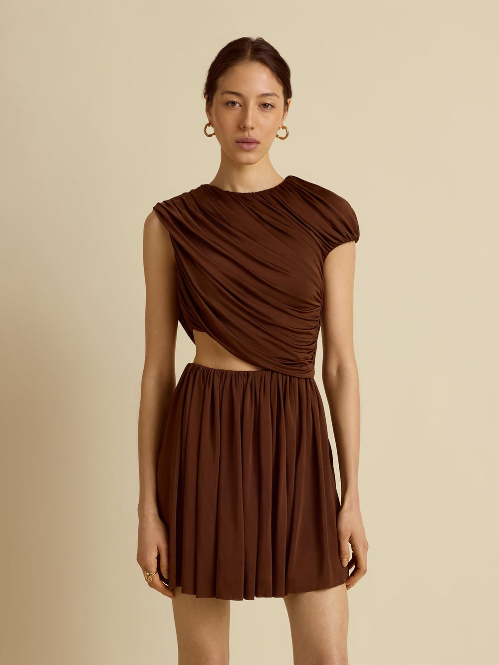Front of Draped Jersey mini dress in umber on model showing draped bodice, side cutout and pleated skirt on beige background