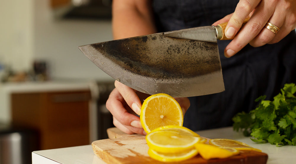 Person slicing lemons with a Thai chef’s moon knife on a wooden cutting board in a kitchen