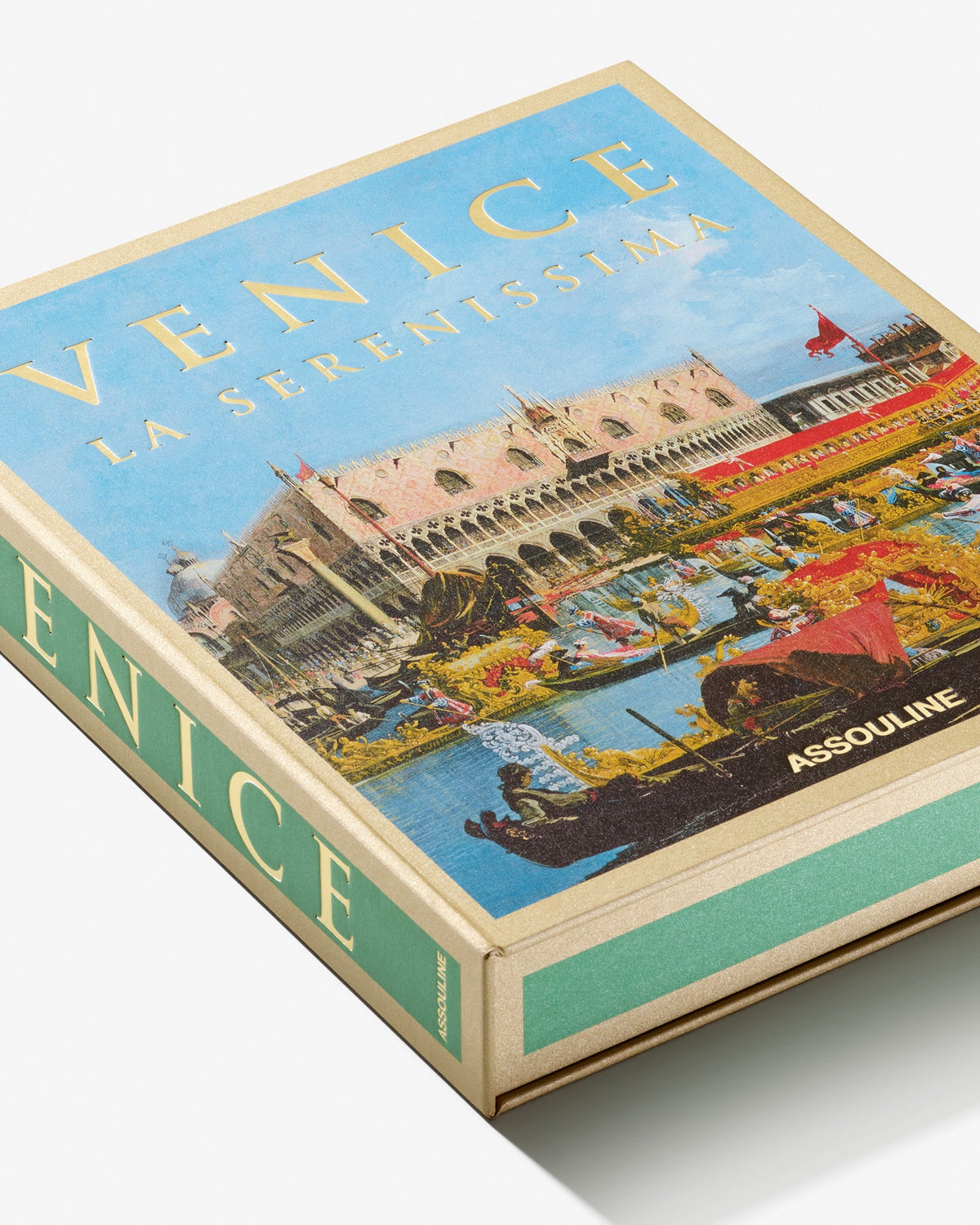 Venice: La Serenissima by Assouline: Angled overhead view of the closed clamshell box laid flat on a white surface. The box top shows the full Canaletto-style painting — VENICE in gold at top, LA SERENISSIMA below, ASSOULINE at lower center. The green-accented spine is visible at right with VENICE printed vertically.
