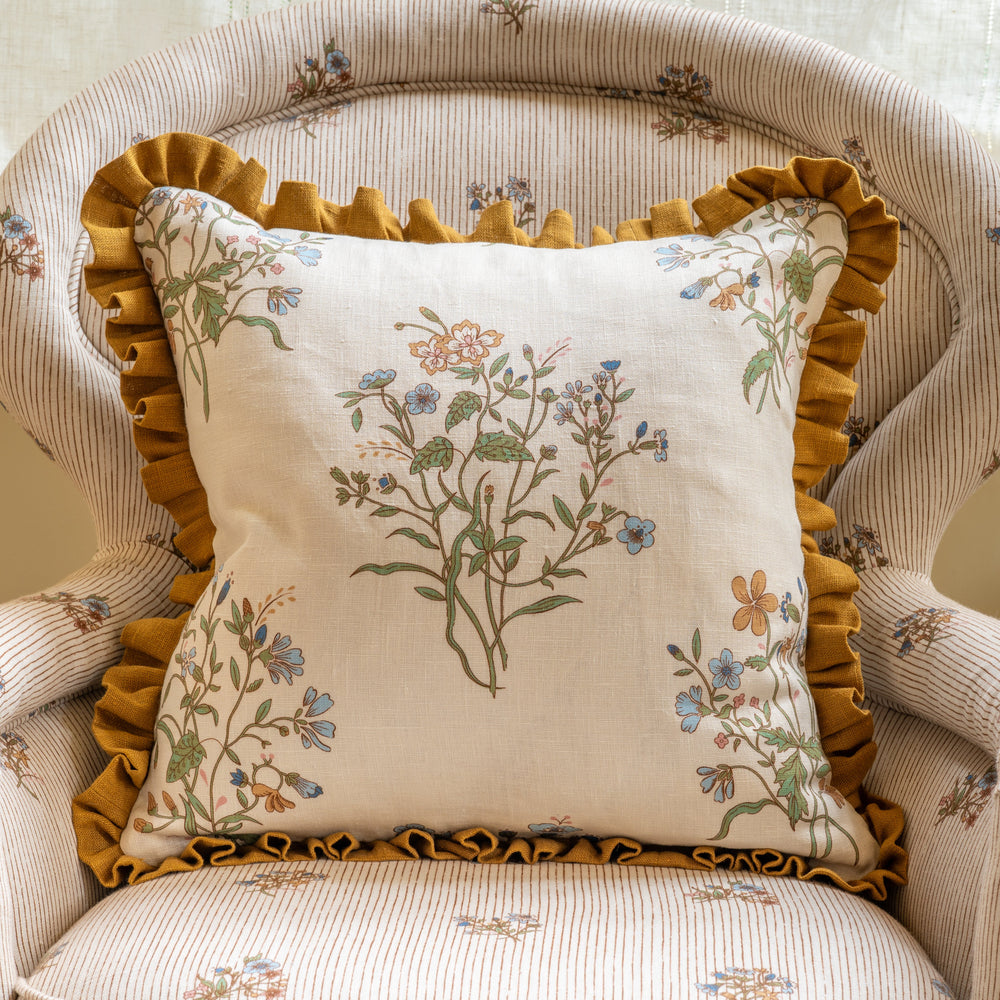 Front view of Flax & Field Flower Print Cushion showcasing Multi/Oyster floral linen and Old Gold frill in a striped armchair