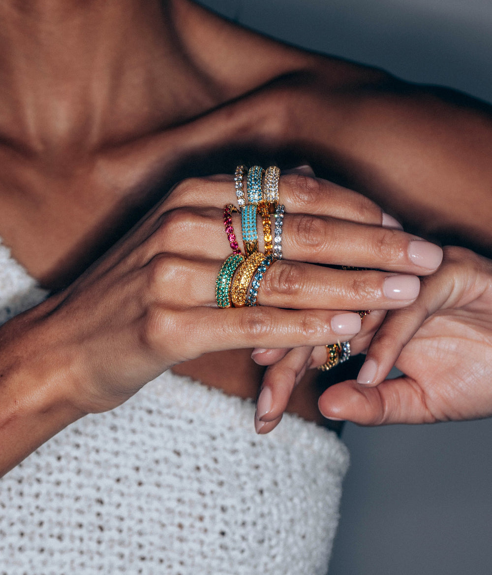 Close-up of hands wearing Veyra ring in smoked sapphire and stacked colored pavé bands showcasing sparkling CZ stones on a model against a gray background