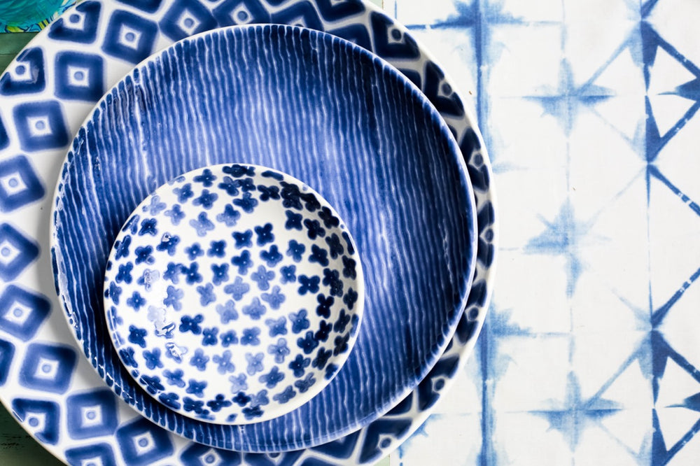 Top view of Santorini Stripe pasta bowl showing hand-painted blue and white stripes on ceramic, stacked on patterned plates