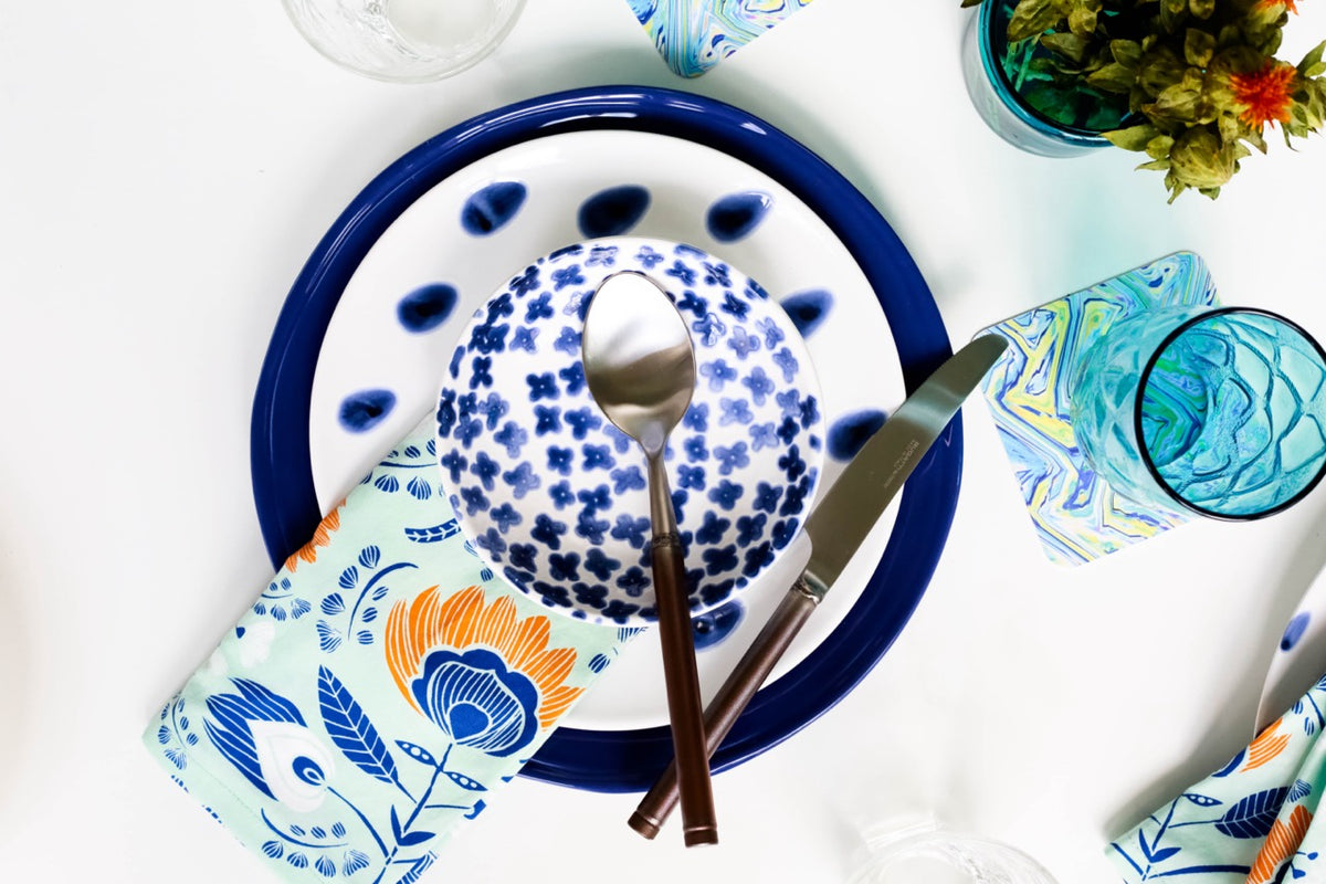 Top view of Santorini 12-piece place setting with blue-and-white patterned bowl, blue-rimmed plate, floral napkin, and cutlery
