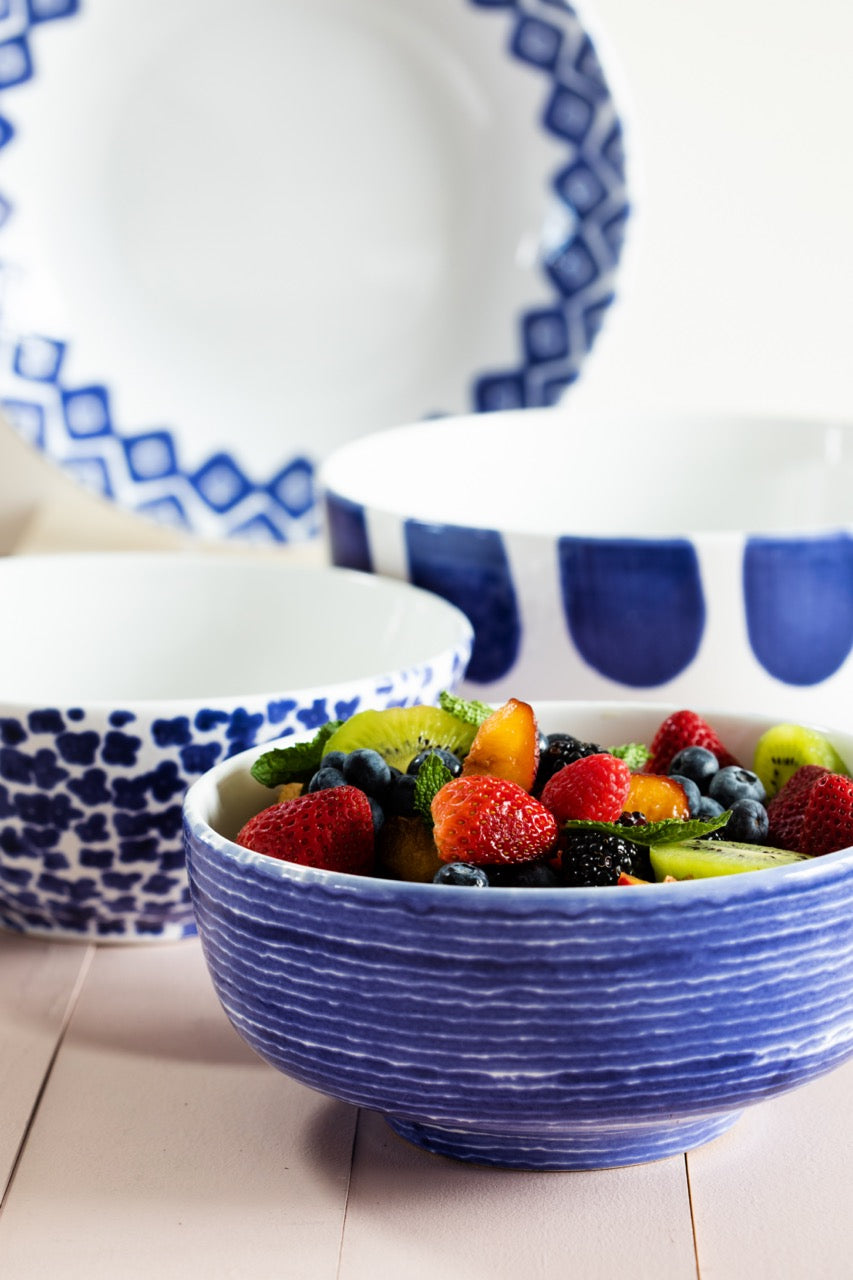 Close-up of Santorini serving bowls set with blue hand-painted patterns and textured glaze, front bowl filled with mixed fruit