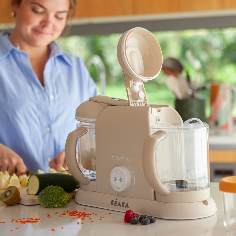 Front view of Babycook Duo in Oat showcasing its two cooking bowls with a woman preparing food in a kitchen