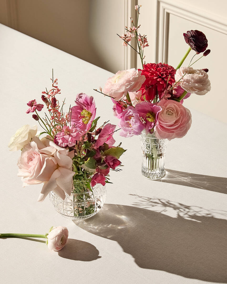 Angled view of Powerscourt 6in crystal vase showing deep cross-cut grid pattern with pink flowers on a light table