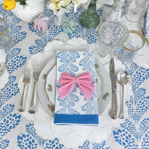 Dining table setting with floral tablecloth, plates, cutlery, and a pink bow on a napkin. white vegan leather luxury placemat. 