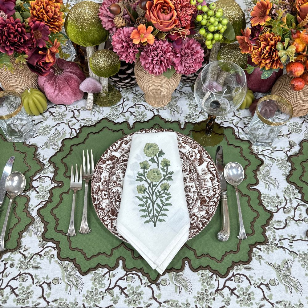 Decorative table setting with floral arrangements, green luxury embroidered placemats, motif green floral napkin and patterned plates.
