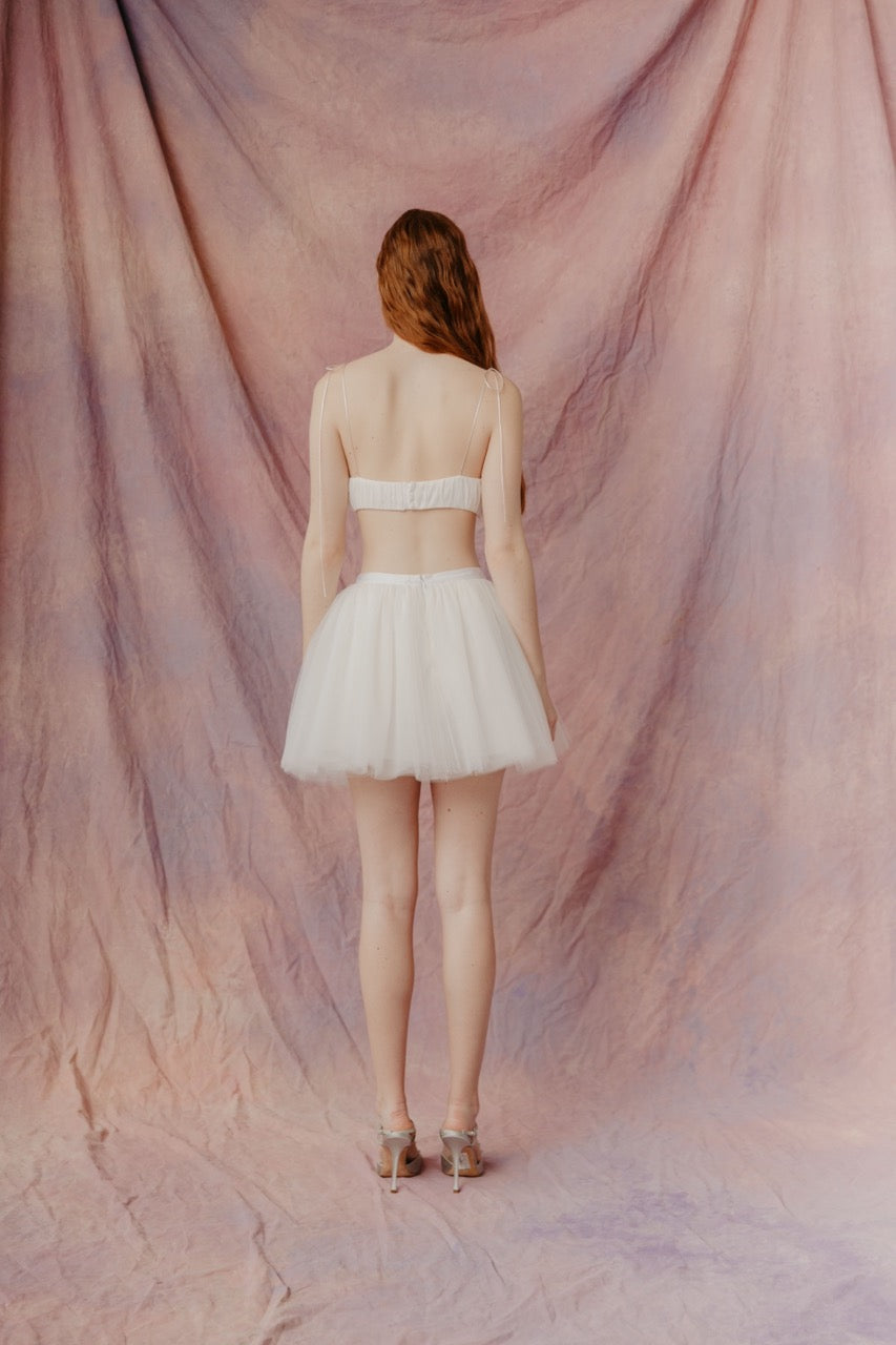 Back view of Willie Top in ivory on model showing thin tie straps and smocked back band against a mottled pink backdrop