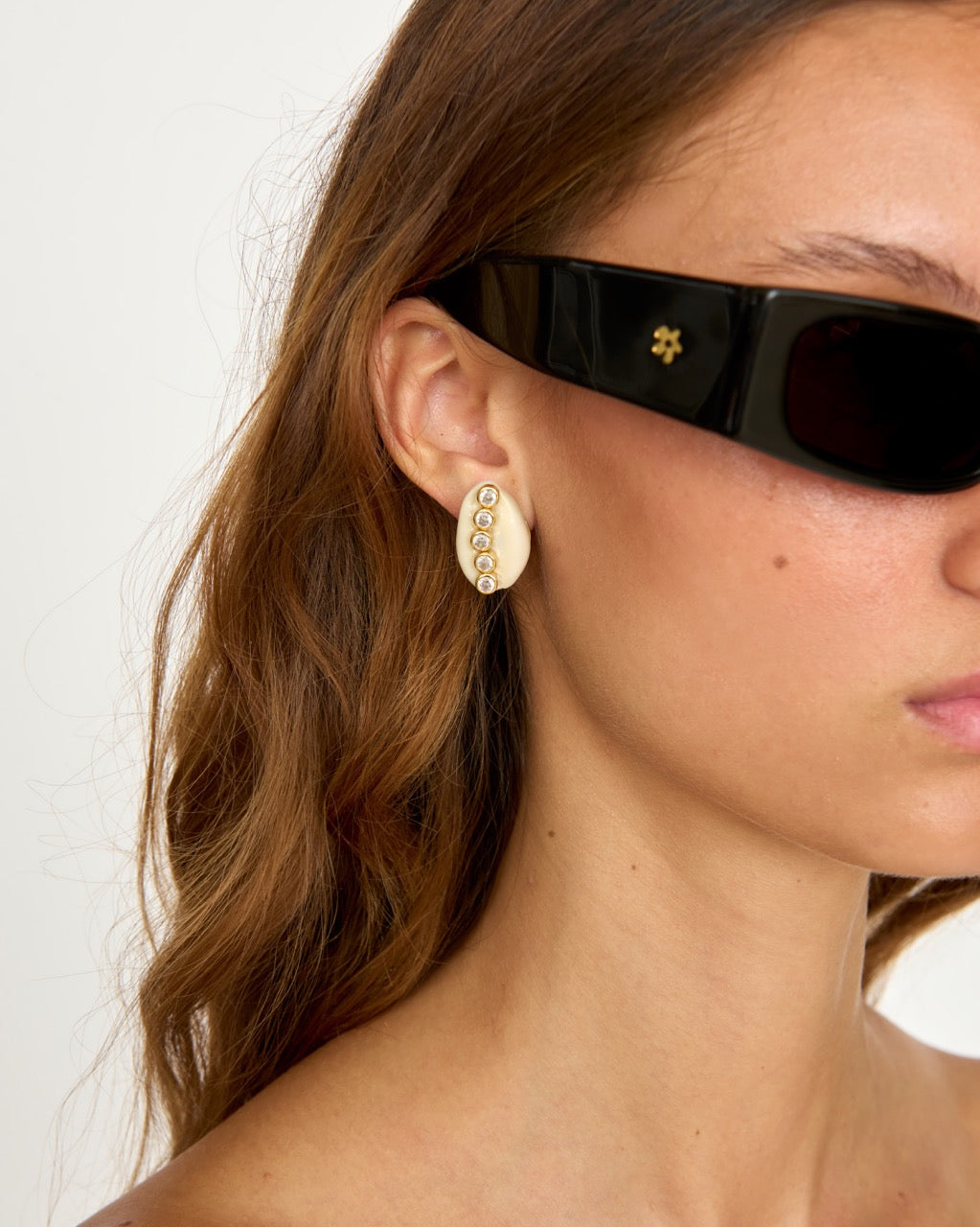 Close-up side view of Wren Earrings showcasing a cowrie shell and cubic zirconia with a model wearing sunglasses
