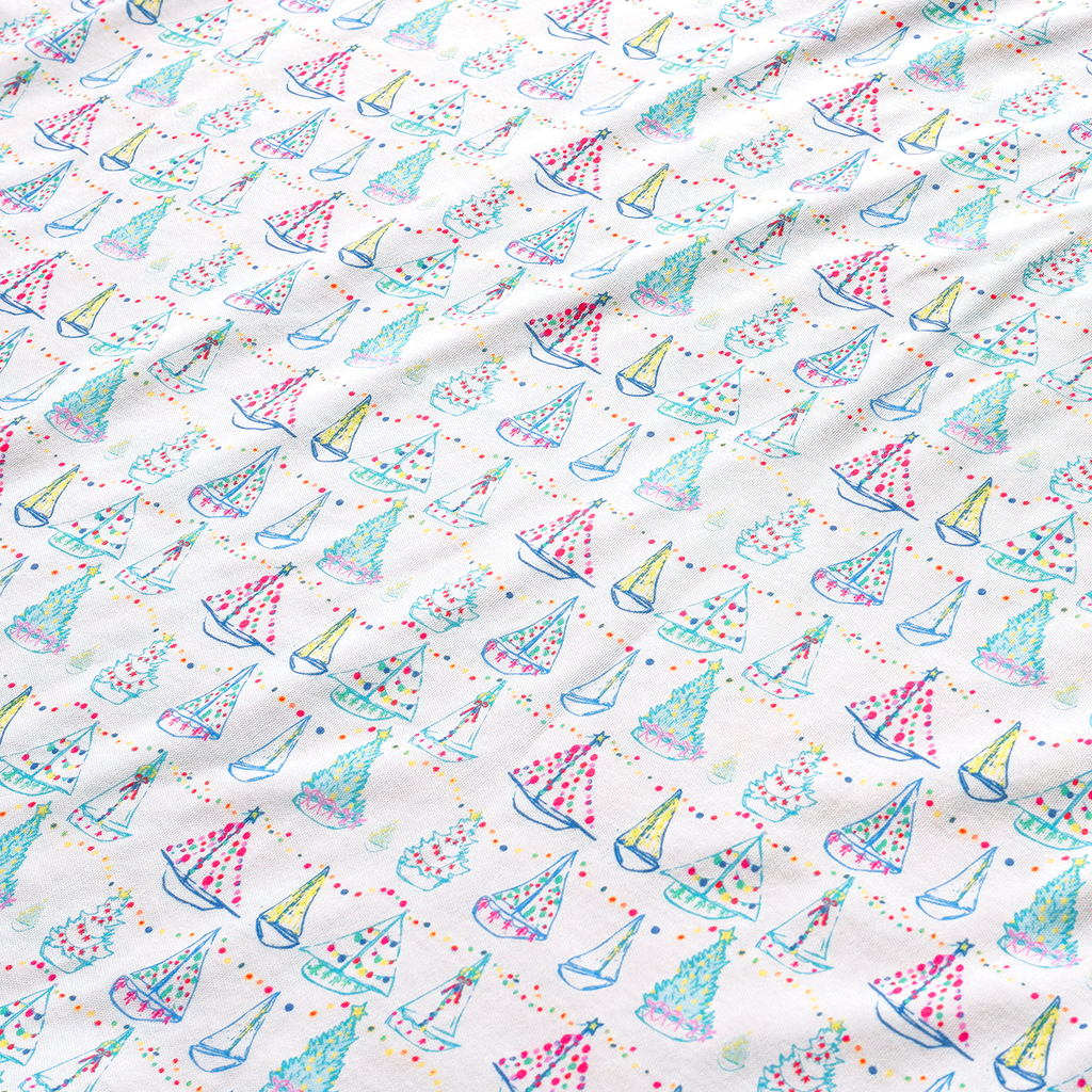 Close-up of Holiday Harbor Zip Baby Onesie with sailboats, colorful lights, garlands, and Christmas trees on white fabric