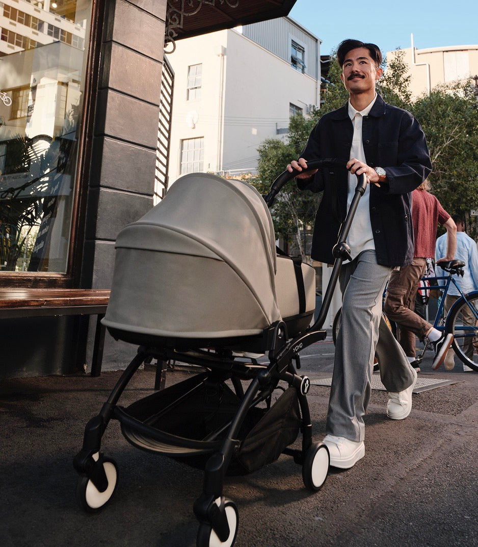 Man pushing YOYO³ 0+ stroller with Stone newborn pack on a city sidewalk
