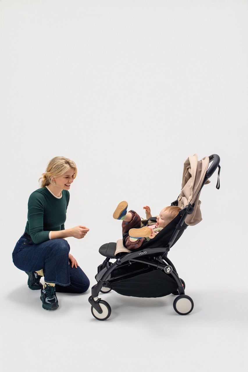 Woman kneeling beside a YOYO stroller as a baby reclines using an attached black leg rest
