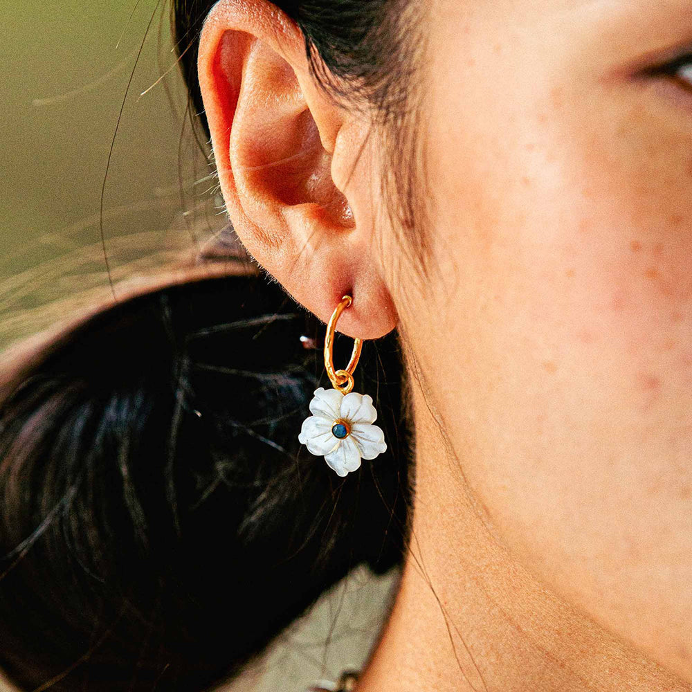 Close-up of ear wearing Mermaid Garden hoop earring showcasing white mother-of-pearl flower charm on gold hoop