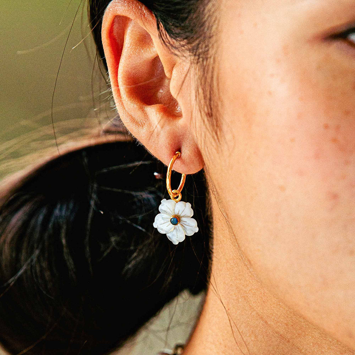 Close-up of ear wearing Mermaid Garden hoop earring showcasing white mother-of-pearl flower charm on gold hoop