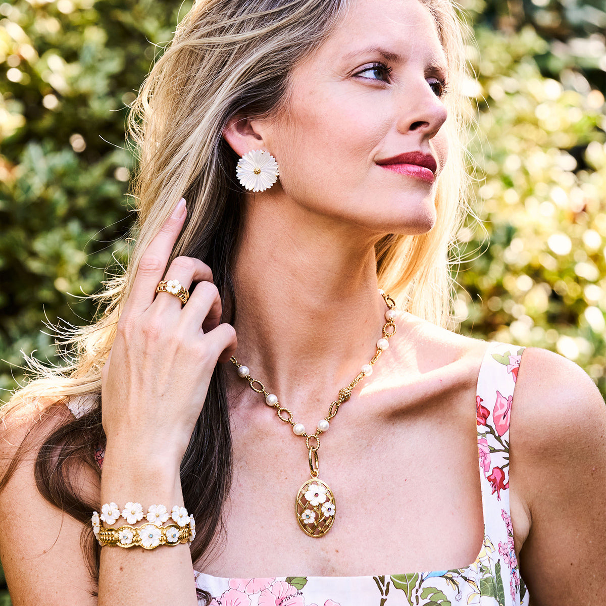 Close-up of Mermaid Garden Blossom stud earrings showing mother-of-pearl flowers with gold centers on model in a garden