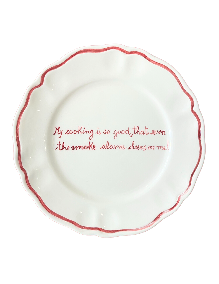 Top view of scalloped ceramic plate showcasing red hand-painted rim and centered handwritten message on black background