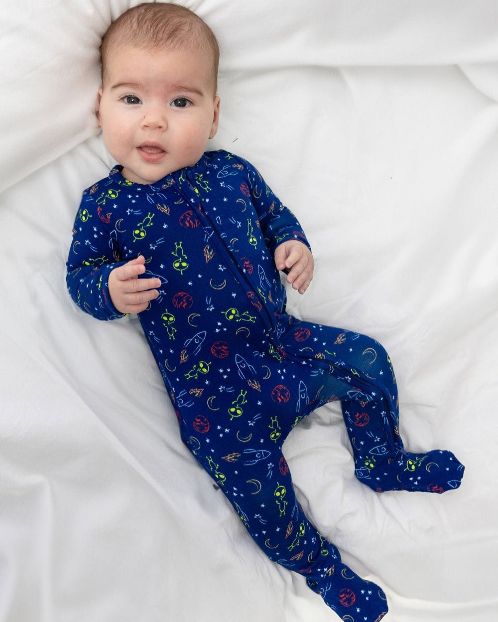 Top view of baby in navy Alien Bamboo Zipper Footie showing two way zipper and grippy footies on white bedding