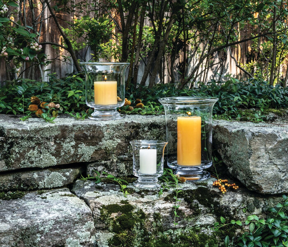Revere Hurricane glass hurricanes arranged with lit pillar candles on a mossy stone wall in an outdoor garden setting