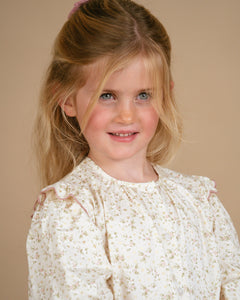 Young girl wearing a white lace dress against a beige background