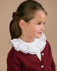 Young girl wearing a red cardigan with a white lace collar against a beige background