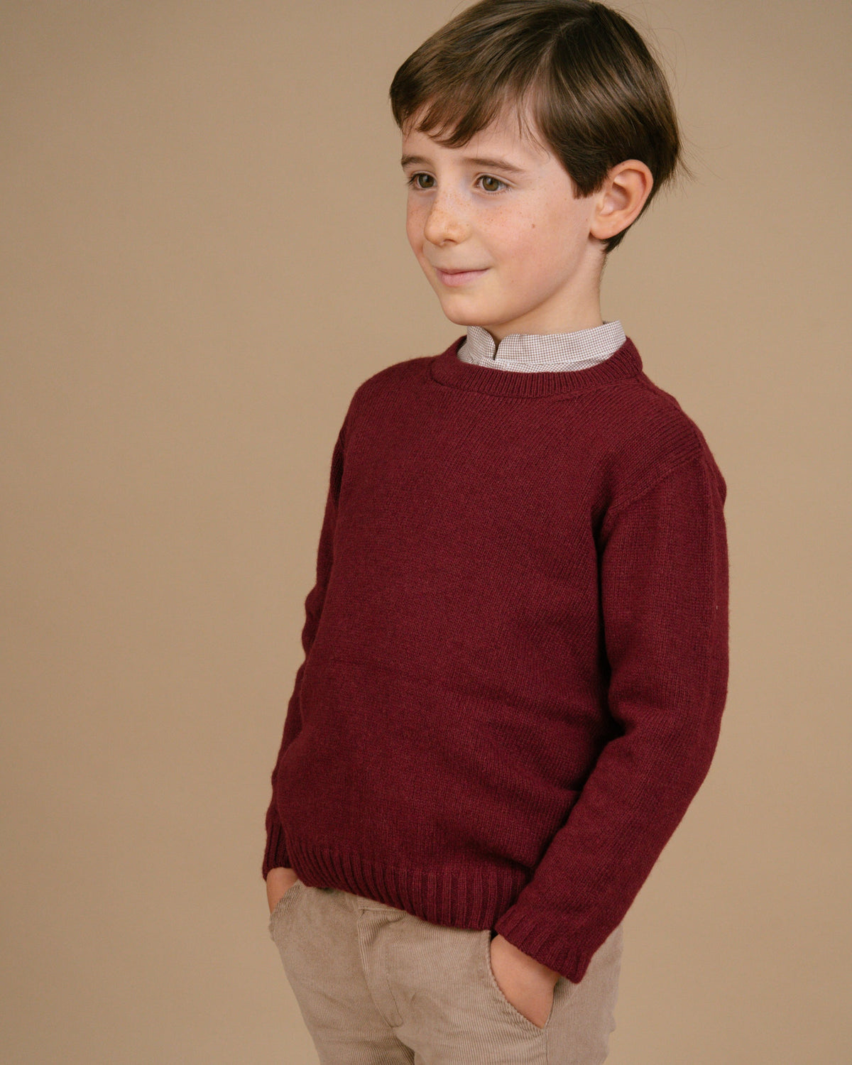Child wearing a maroon sweater against a beige background