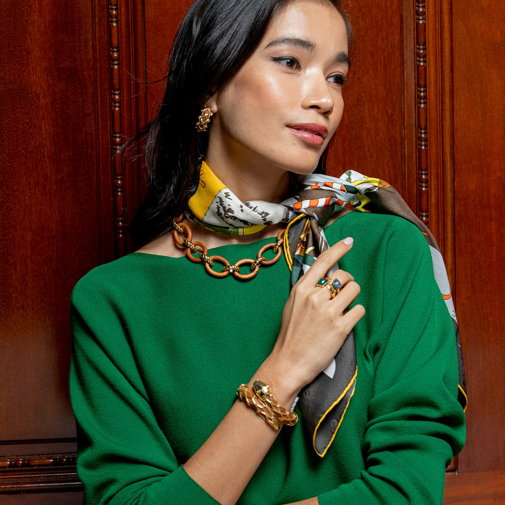 Woman in green sweater wearing gold necklace, bracelet, and a blue labradorite ring with scarf against wood paneling