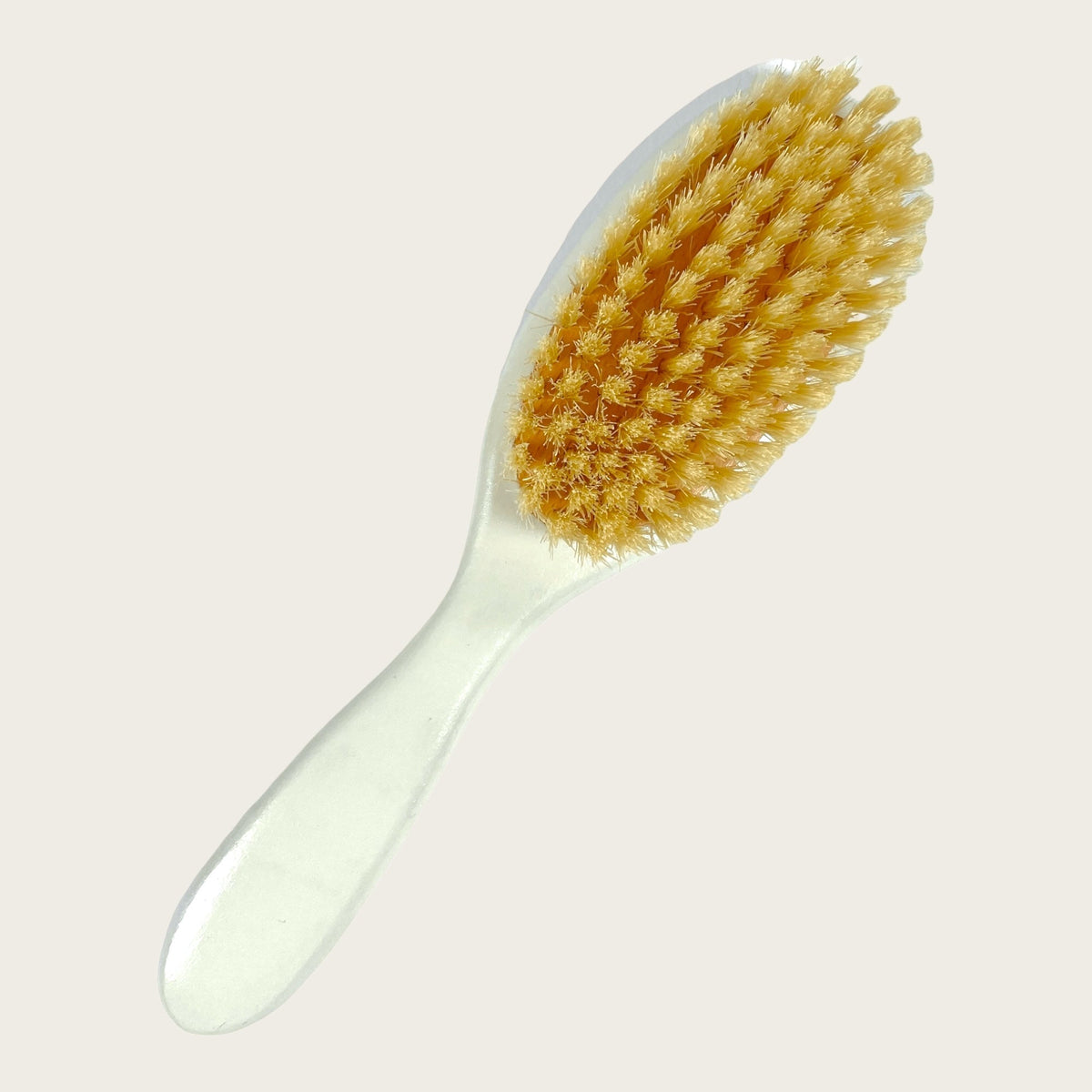 Angled top view of baby brush showing yellow natural bristles and white hand-painted beech wood handle on pale background