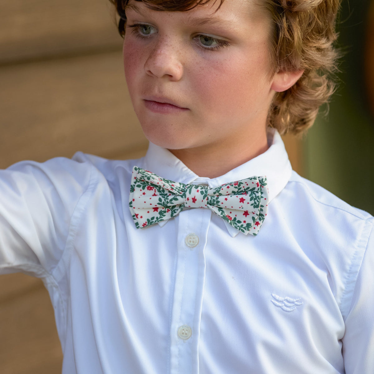 Front view of Baker Bow Tie in Regent Wreaths showcasing its festive wreath print on a boy wearing a white shirt