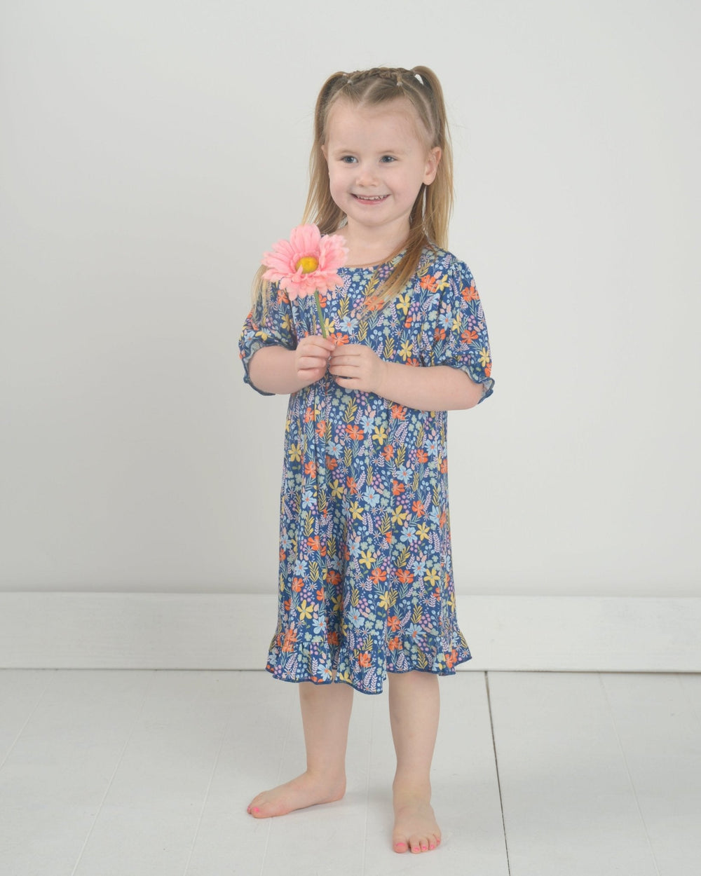 Front view of girl’s bamboo nightgown with navy floral print, ruffle hem and short sleeves on a child against a light gray background