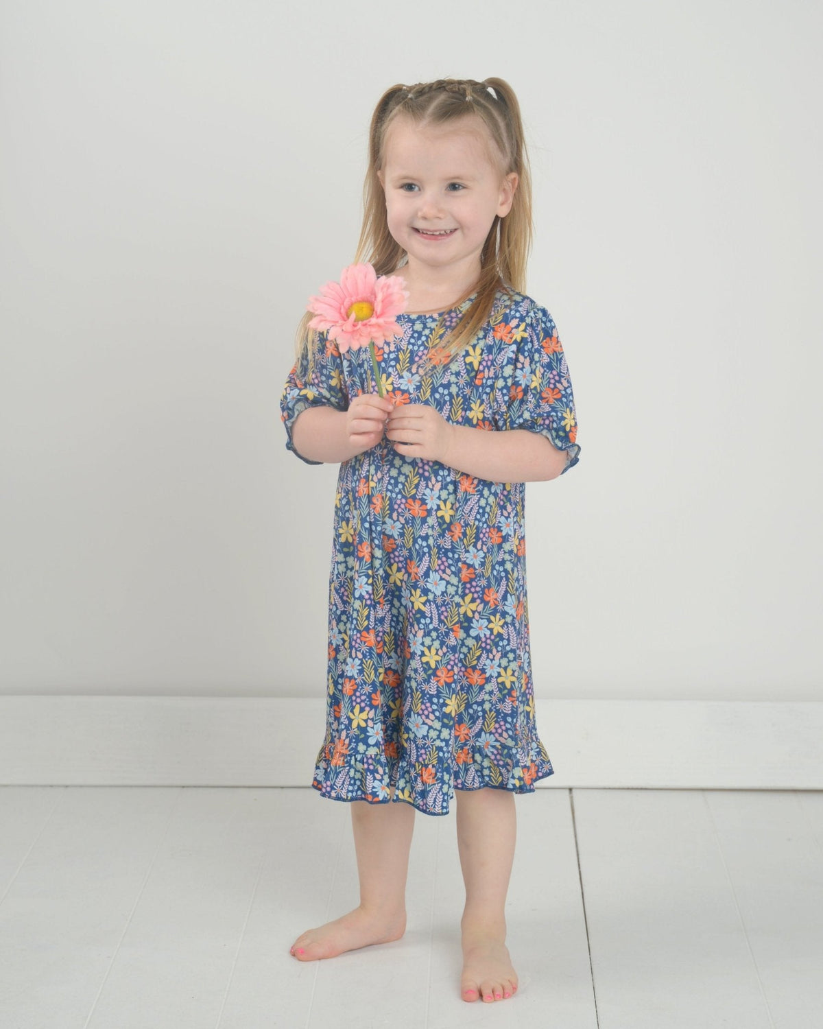 Front view of girl’s bamboo nightgown with navy floral print, ruffle hem and short sleeves on a child against a light gray background