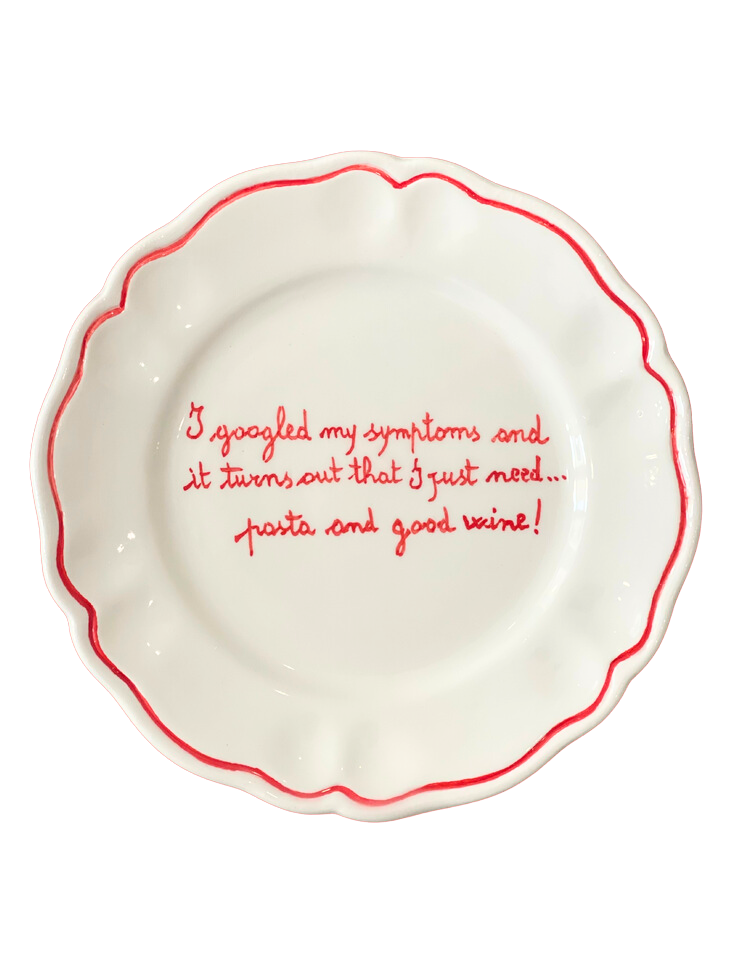 Top view white scalloped ceramic plate with red rim and handwritten joke about needing pasta and wine on black background