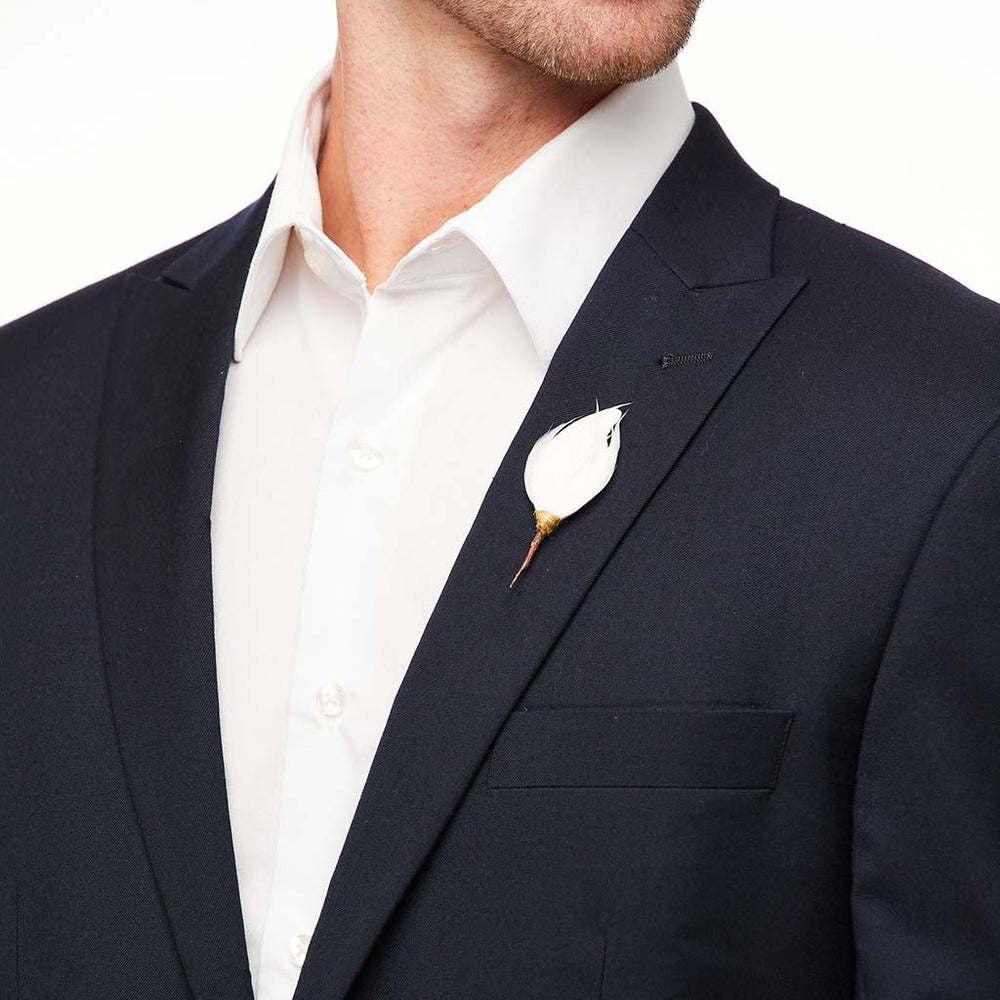 Close-up of Beckham lapel pin showing a white goose feather with a gold stem pinned to a navy suit lapel