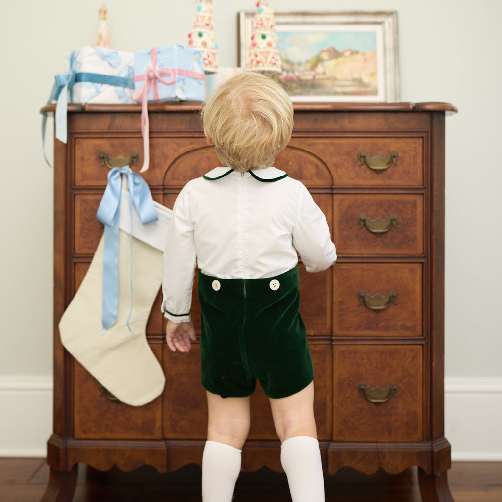Back view of Benjamin Button On in Grafton Green Velvet showing green velvet shorts and white top with a dresser background