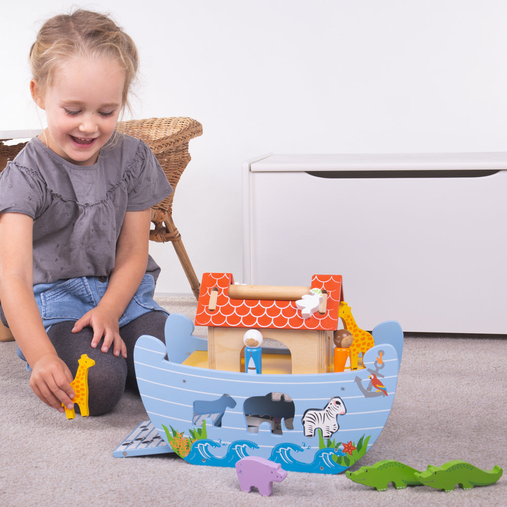 Front view of colorful 16-piece wooden Noah’s Ark toy showcasing animal figures and fold-down ramp with a child beside it