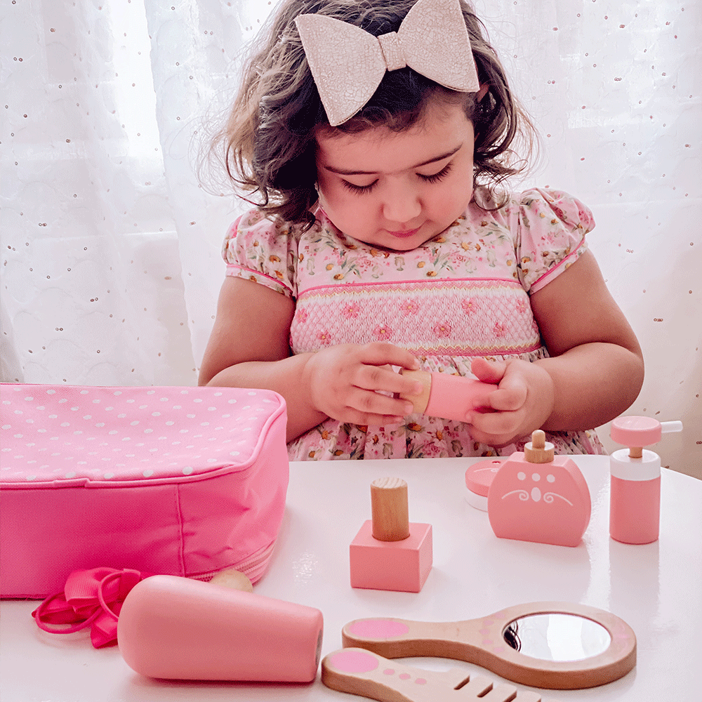 Front view of Vanity Kit showcasing wooden beauty accessories and pink carry bag while a child plays with the set