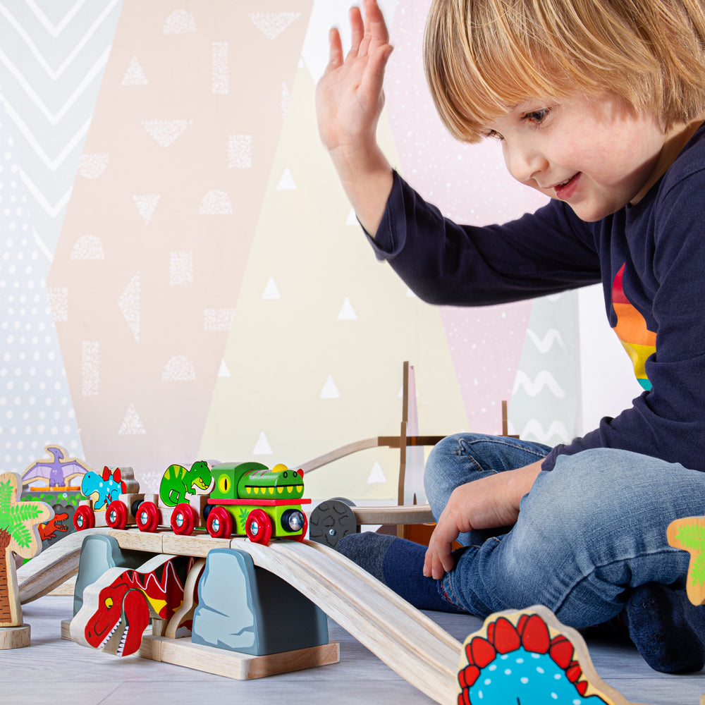 Front view of T-Rex Bursting Bridge showcasing dinosaur-themed wooden train tracks with a child playing in the background
