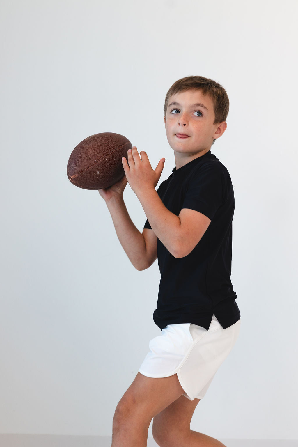 Side view of Practice Shirt in Black on a child showing athletic fit and short sleeves with white shorts on white background