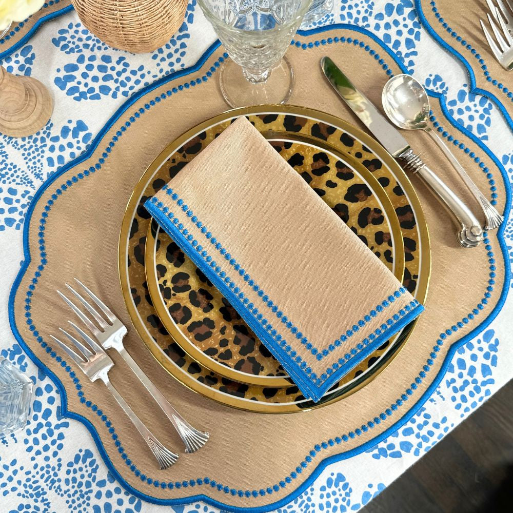 Table setting with leopard print plates, gold charger, and blue napkin on a patterned tablecloth.